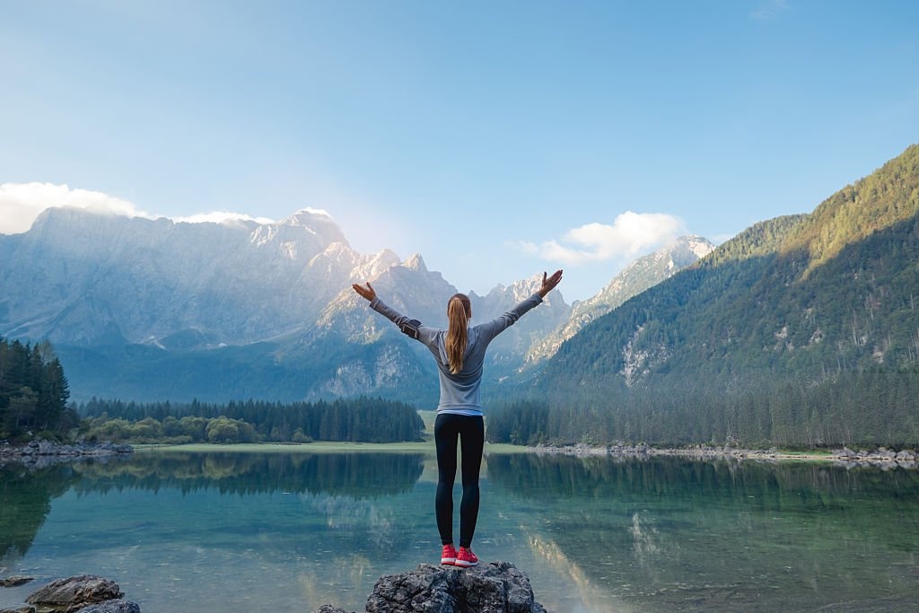 Person standing by a mountain lake with arms raised
